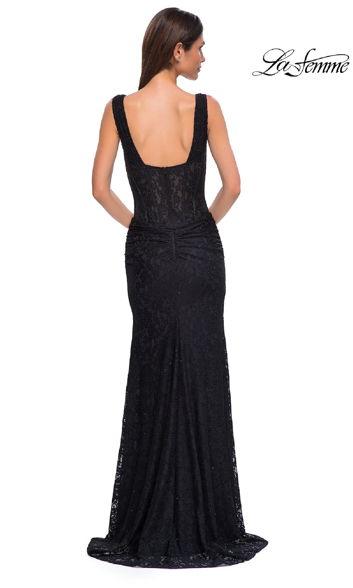 A woman stands facing away, wearing the La Femme 32943 beaded long lace prom dress. This fitted black sleeveless gown features a low open back and hugs her waist and hips before flaring elegantly at the hem.